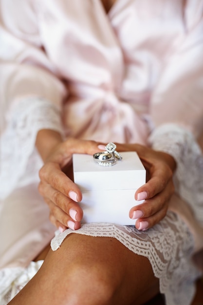 Wedding rings made of white gold and diamonds lie on white box in bride's arms