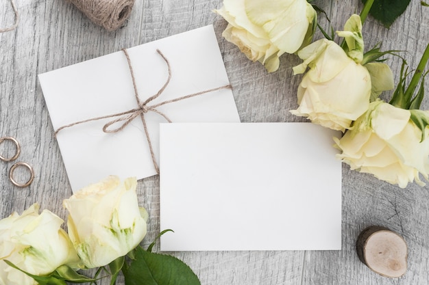 Wedding rings; roses and two white envelopes on wooden backdrop