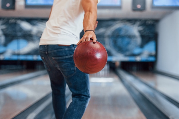 Weekend activities. Rear particle view of man in casual clothes playing bowling in the club