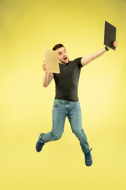 Weightless. Full length portrait of happy jumping man with gadgets isolated on yellow background