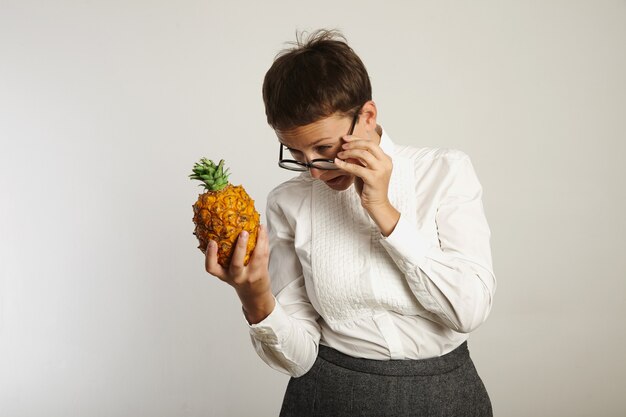 Weird looking female teacher squinting at a pineapple above glasses isolated on white