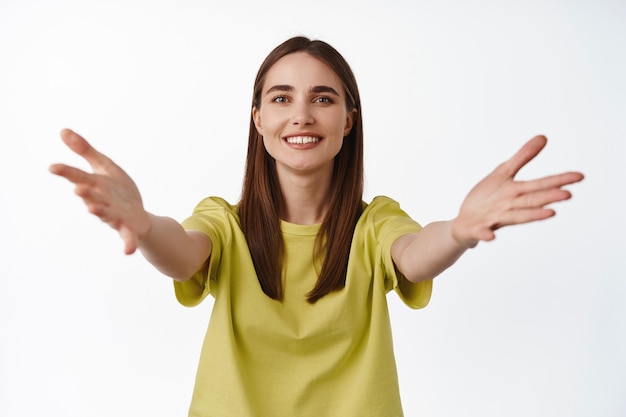 Welcome. Smiling friendly girl reaching for hugs, spread hands to hold or receive something, taking in her arms, standing on white