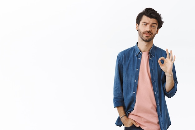 Well not bad but okay Skeptical handsome guy telling how meeting went making OK alright sign as satisfied or feeling fine agree rate something normal standing white background judgemental