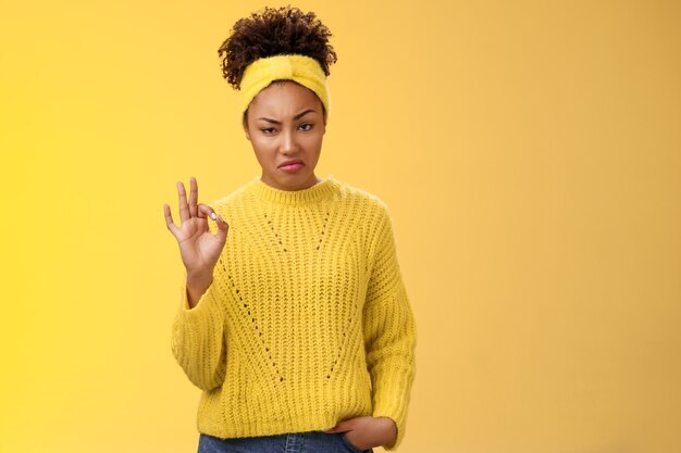 Well not bad. Portrait serious-looking confident arrogant young african-american woman agree effort good show okay ok normal gesture smug approval, standing yellow background impressed. Copy space