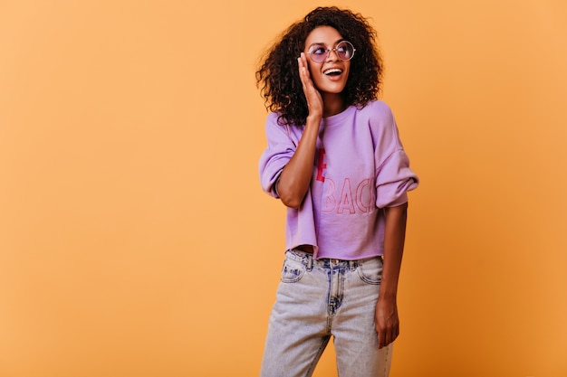 well-dressed girl looking around with smile. Romantic curly african woman smiling on orange.