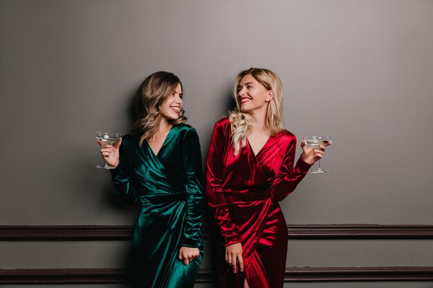 Well-dressed girls looking at each other while drinking wine. Laughing friends enjoying conversation.