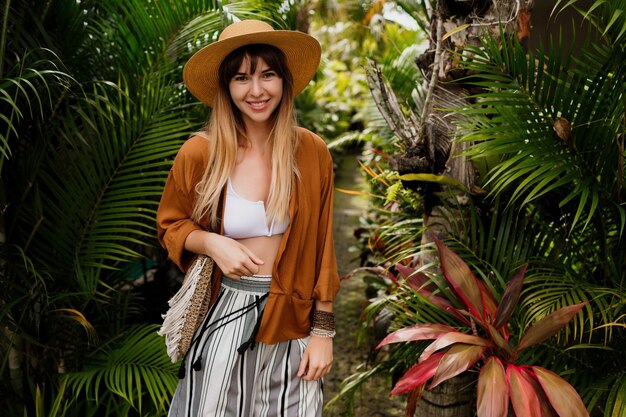 Well-dressed woman in perfect mood playfully posing in tropical garden.