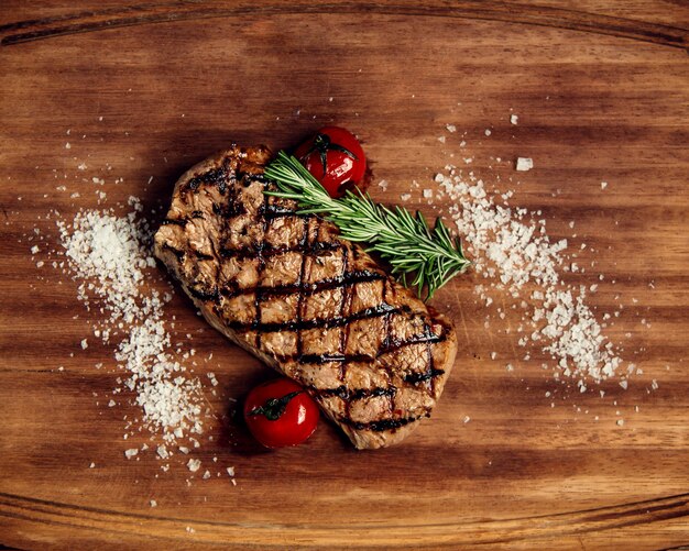 Well-fried piece of steak and tomatoes on a wooden board