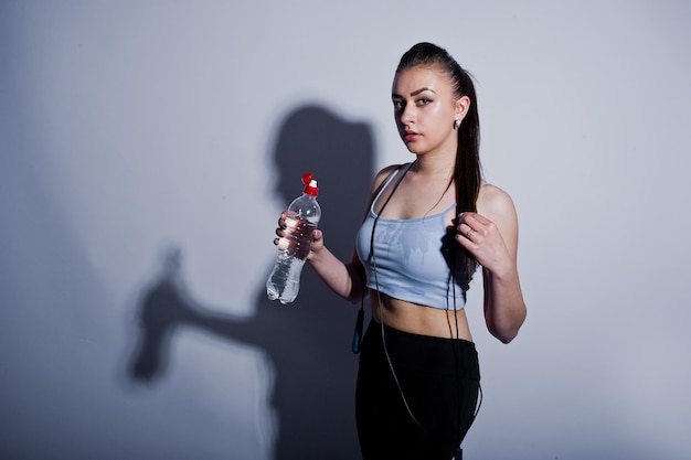 Wet cheerful attractive young fitness woman in top and black leggings with jump rope and bottle of water isolated over white background