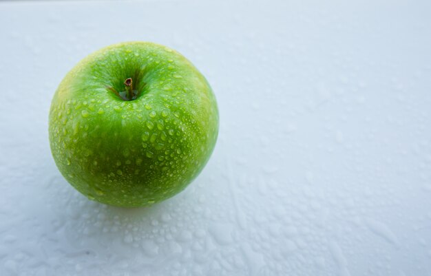 Влажное зеленое яблоко на взгляде белизны, высокого угла.