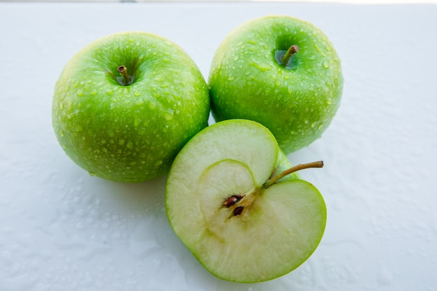 Wet green apples and half on white. close-up.