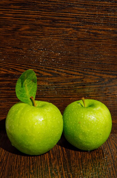 Wet green apples with leaf on curved dark wood. side view.