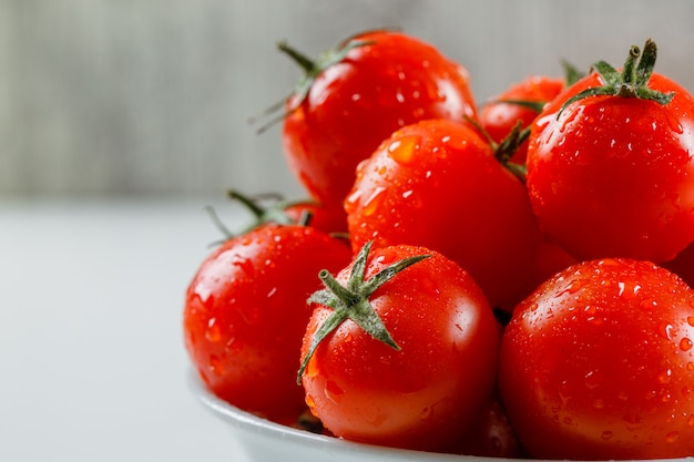 Wet juicy tomatoes in a white plate on a white and grungy surface. side view.