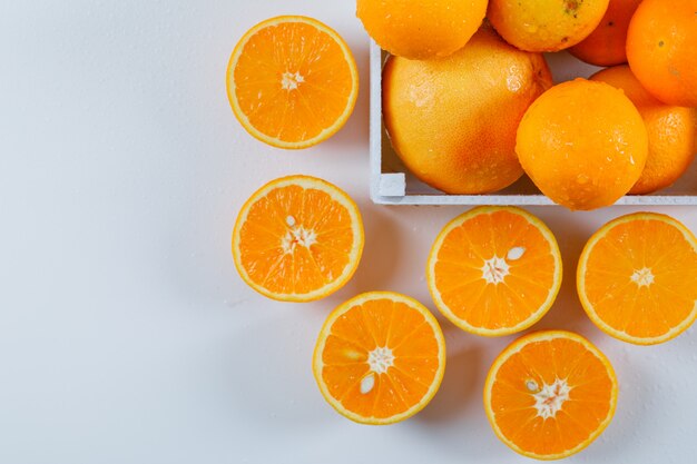 Wet oranges with halves in a white rectangle bowl on a white surface. high angle view.