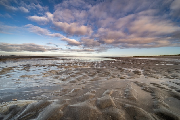 Wet shore with small water puddles under a blue cloudy sky