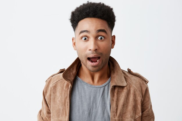 What. Close up of young shocked black-skinned man with afro hairstyle in casual stylish outfit looking in camera with opened mouth and raised eyebrows, being surprised win lottery.
