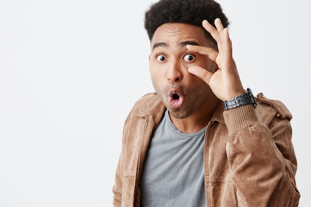 Free photo what the heck is going on. close up of young dark-skinned man with afro haircut in casual stylish clothes being shocked seeing friend on new expensive car. man feeling envy.