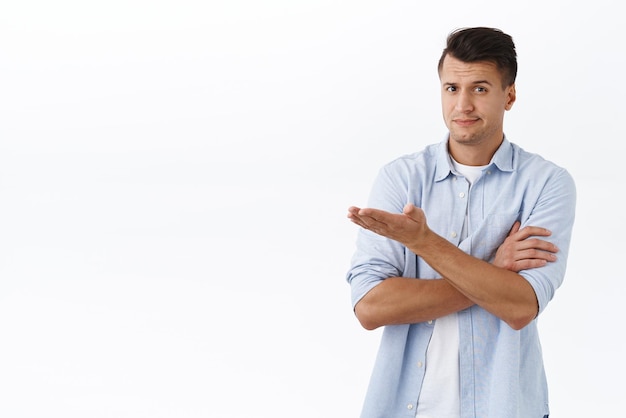 What the hell is this Portrait of skeptical disappointed handsome man smirk judgemental and pointing hand left at blank white space raise eyebrow bothered with unsatisfying product