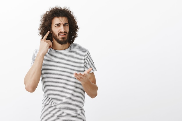 Foto gratuita quello che non riesco a sentirti, cosa vuoi. ritratto di ragazzo orientale bello infastidito confuso con acconciatura afro, dirigendo all'orecchio e indicando con il palmo