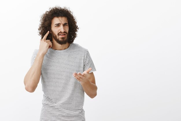 What I cannot hear you, what do you want. Portrait of confused bothered handsome Eastern guy with afro hairstyle, directing at ear and pointing with palm