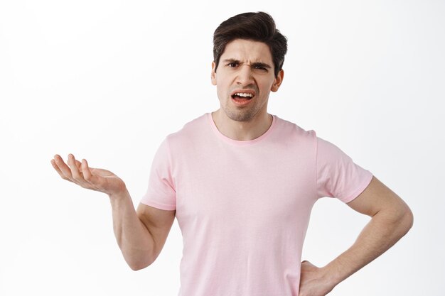 What is that. Frustrated and confused man raise hand and stare puzzled, cant understand wtf happening, standing bothered and questioned against white background