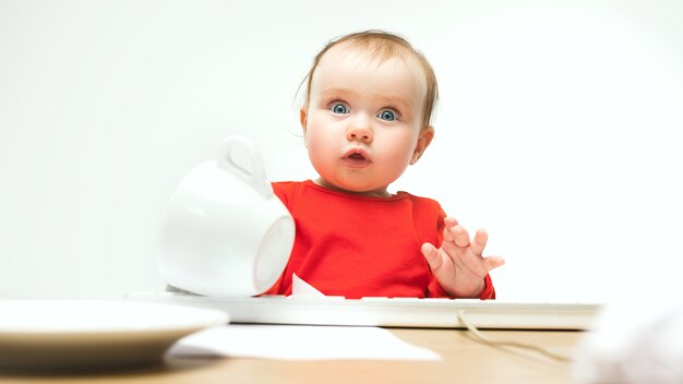 흰색 스튜디오에서 현대 컴퓨터 또는 노트북의 키보드와 함께 앉아 무슨 놀란 아이 아기 소녀