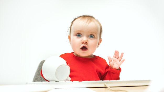 What Surprised child baby girl sitting with keyboard of modern computer or laptop in white studio