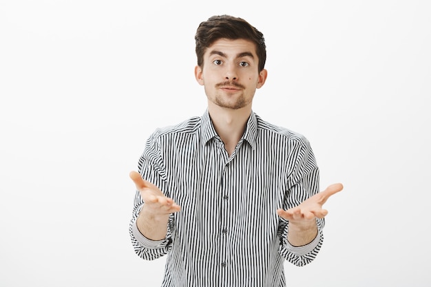 What do you want from me. Portrait of annoyed tired handsome bearded guy in striped shirt, pulling hands towards