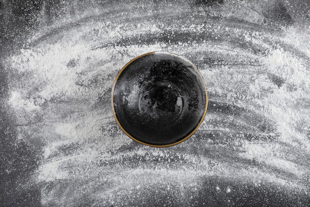 Wheat floor spilled on black surface and empty black bowl