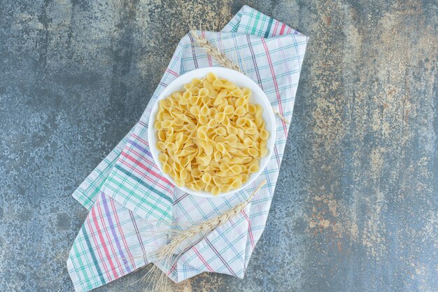 Wheat spike next to a bowl of farfalle pasta , on the marble surface. 