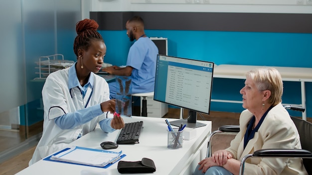 Wheelchair user and doctor analyzing radiography results at medical consultation in cabinet. Medic explaining x ray scan diagnosis to woman with chronic disability, impairment healthcare checkup.