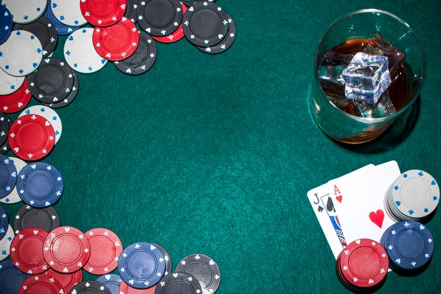 Whisky with ice cubes and casino chips and playing card on green poker table