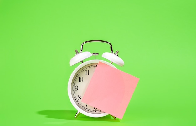 Free photo white alarm clock and blank paper reminder on a green background isolated