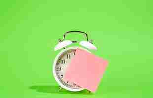 Free photo white alarm clock and blank paper reminder on a green background isolated