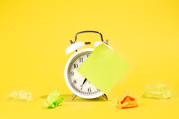 White alarm clock and blank paper reminder on a yellow background isolated