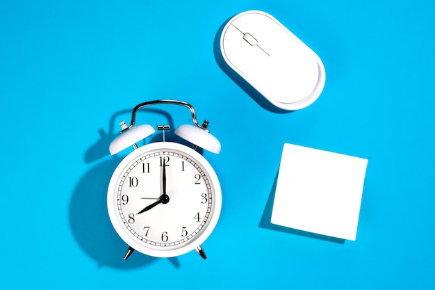Free photo white alarm clock and blank white paper sticker on a blue background isolated