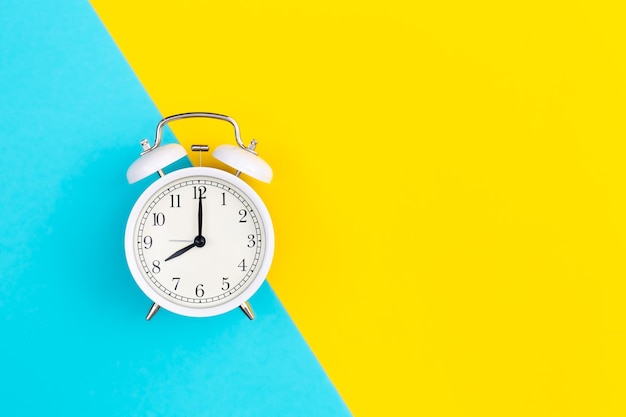 White alarm clock on a blue and yellow background flat lay