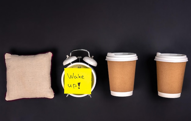Бесплатное фото Белый будильник одноразовые чашки и маленькая подушка на темном фоне