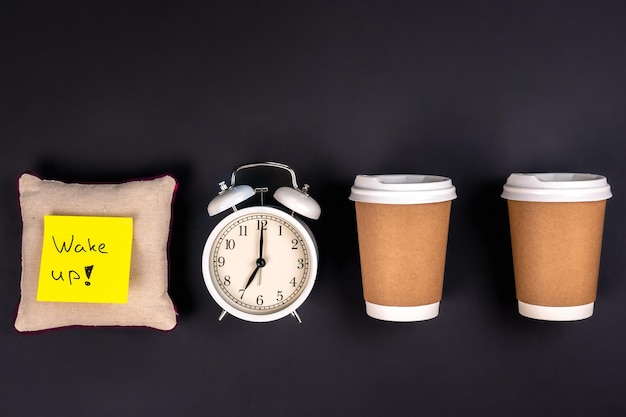 Free photo white alarm clock disposable cups and a small pillow on a dark background