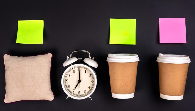 White alarm clock disposable cups and a small pillow on a dark background