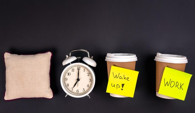 White alarm clock disposable cups and a small pillow on a dark background