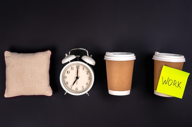 White alarm clock disposable cups and a small pillow on a dark background