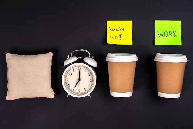 Free photo white alarm clock disposable cups and a small pillow on a dark background