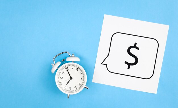 White alarm clock and dollar sign on a blue background flat lay