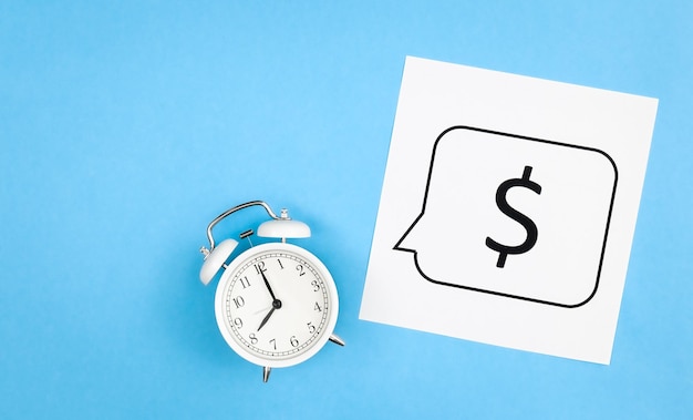 White alarm clock and dollar sign on a blue background flat lay