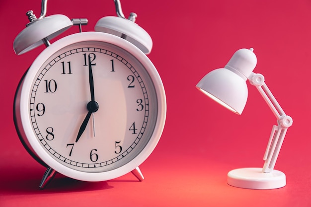 A white alarm clock and a small toy table lamp on a Viva Magenta background