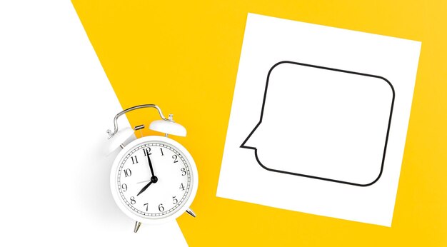 White alarm clock and speech bubble on yellow background flat lay