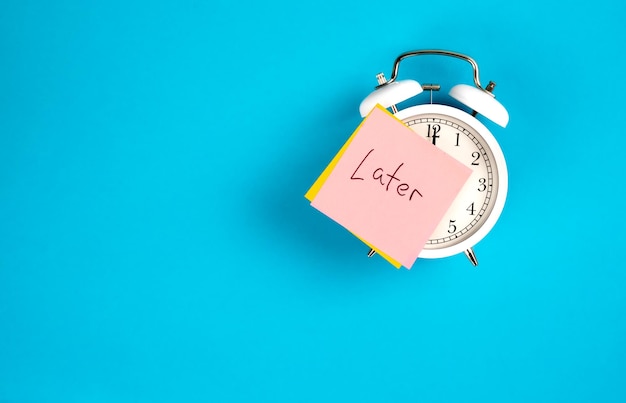 Free photo white alarm clock and sticker with the inscription late on a blue background