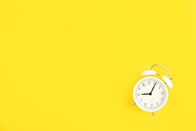 White alarm clock on a yellow background flat lay