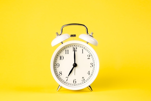 White alarm clock on a yellow background isolated closeup